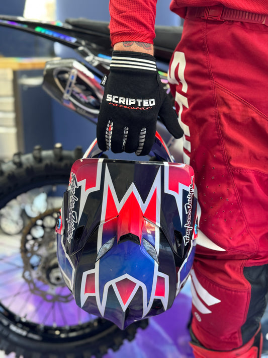 Scripted Clothing Racecraft Multi Use Glove holding a motobike helmet with a bike in the background.